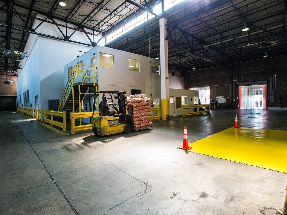 Forklift moving a pallet of produce across a warehouse towards a refrigerated room with strip curtains