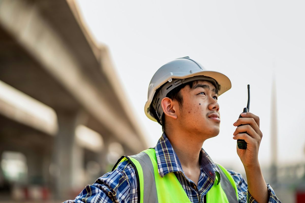 A plant worker in a hard hat talking on a handheld radio