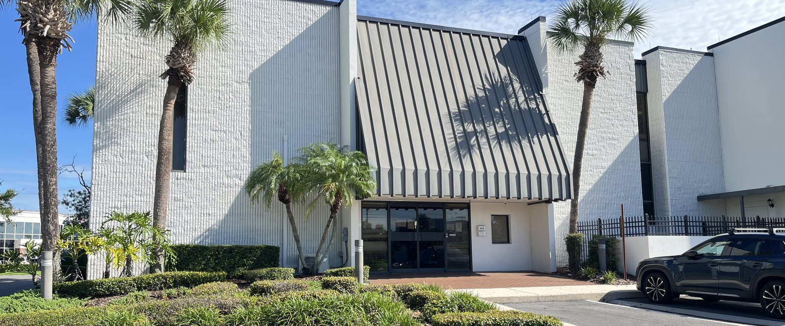 The FLSEMI office building at 400 W Emmett Street, Kissimmee, Florida — white masonry facade with a standing-seam canopy over the entrance, framed by palms